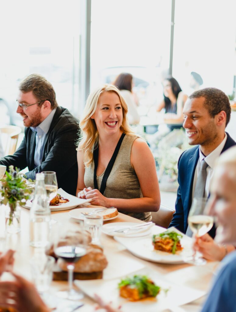 Eventi Business a diverse group of people enjoying a lively dinner party. the scene features men and women of various ethnicities, sharing laughter and delicious food at a beautifully set table.